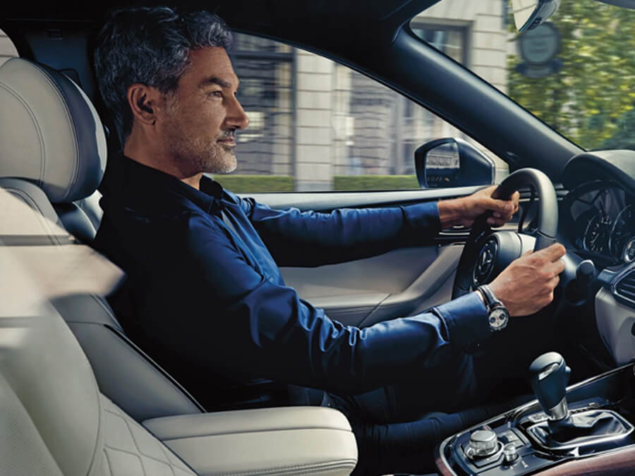 Passenger-side view of middle-aged male wearing blue shirt and silver watch driving down urban street.