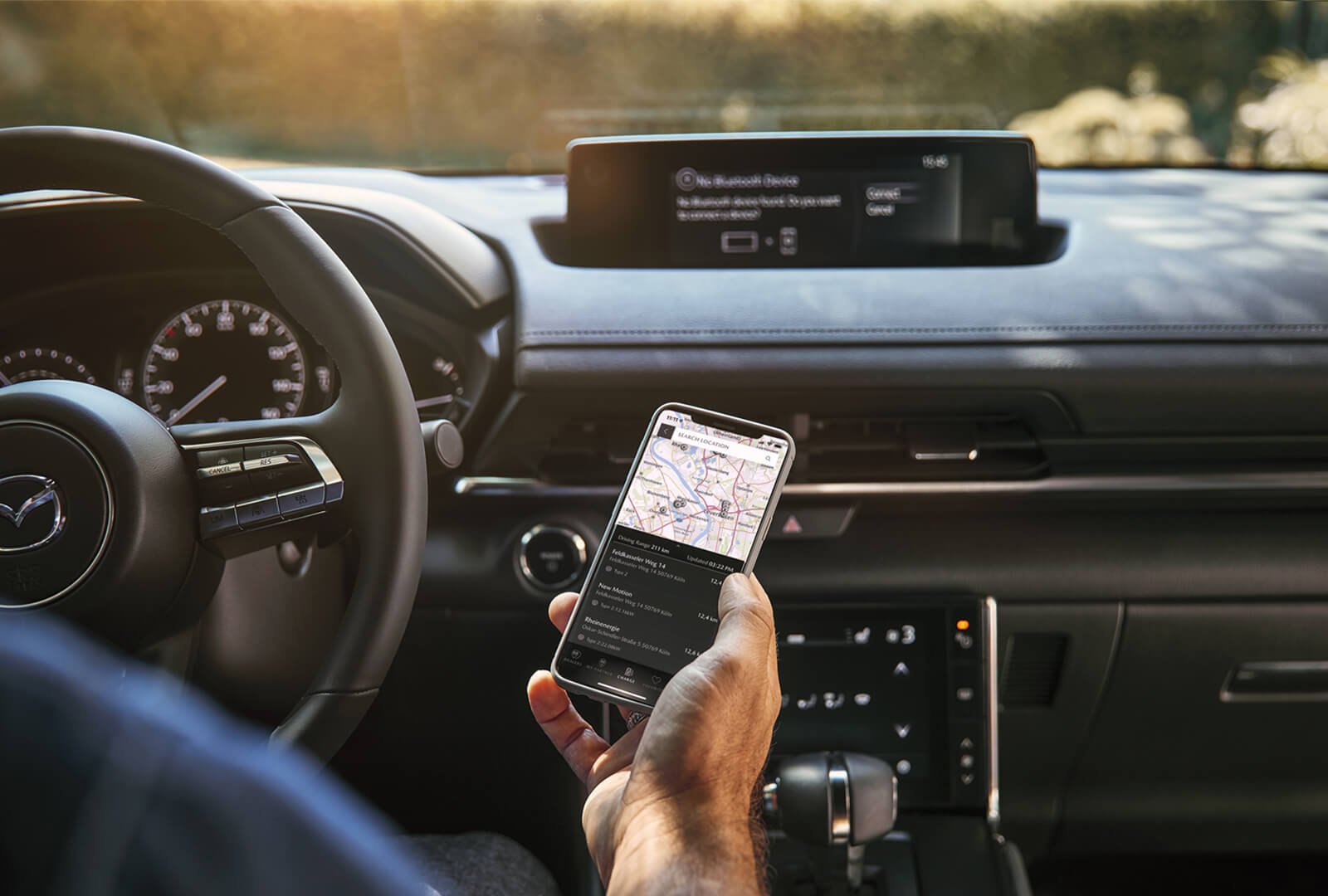 Driver holds a mobile phone with MyMazda app on the screen displaying map