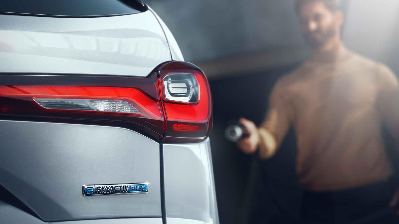 Un conducteur s’approche d’une Mazda avec un chargeur de niveau 2 à la main.