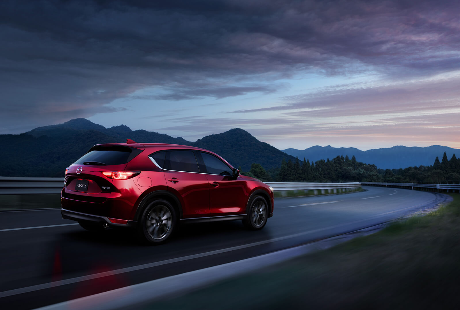 Mazda CX-5 rouge dans un virage sur une route dégagée en direction des montagnes au loin.