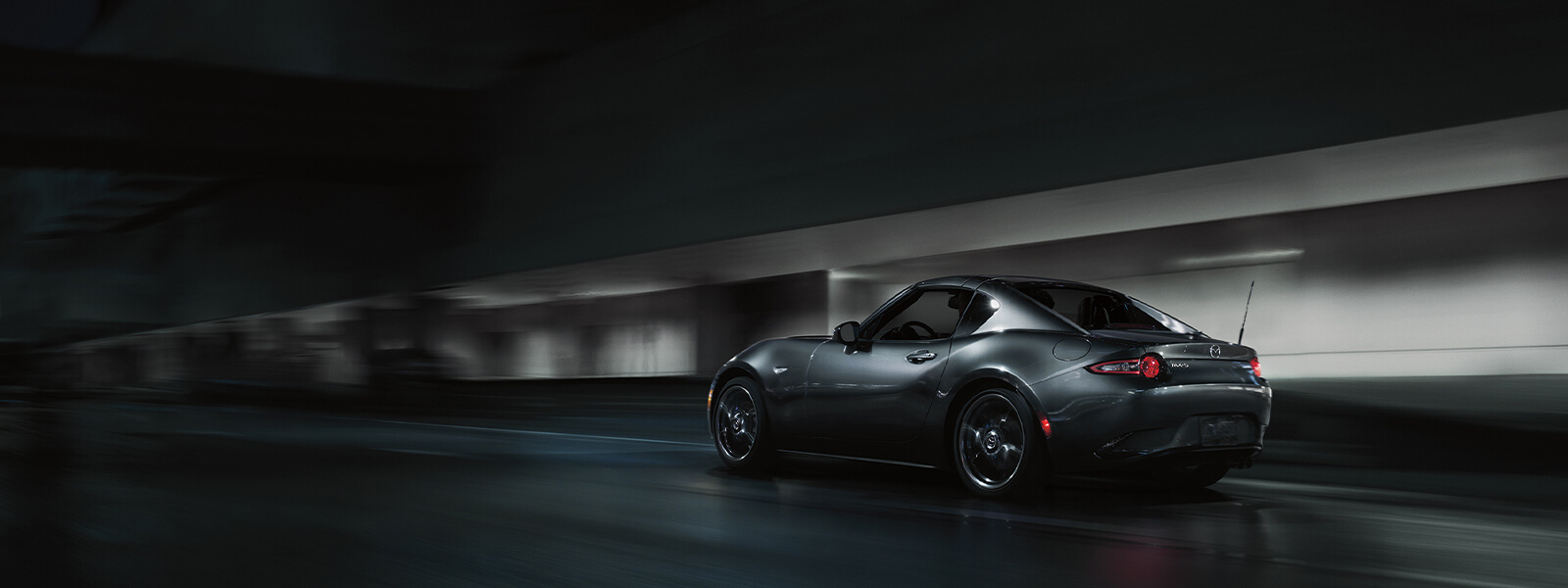 Polymetal Grey Metallic Mazda MX-5 RF hardtop driving along dimly lit urban street.