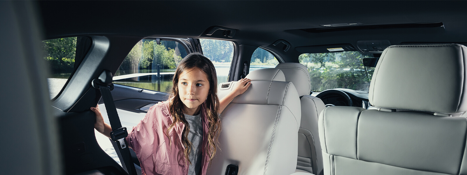 Girl in pink jacket looking through driver side rear passenger door into back compartment of Mazda SUV