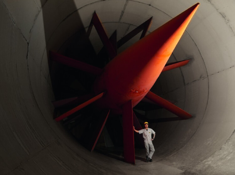 Mazda technician wearing white cap and coveralls standing in the intake of a giant wind tunnel 