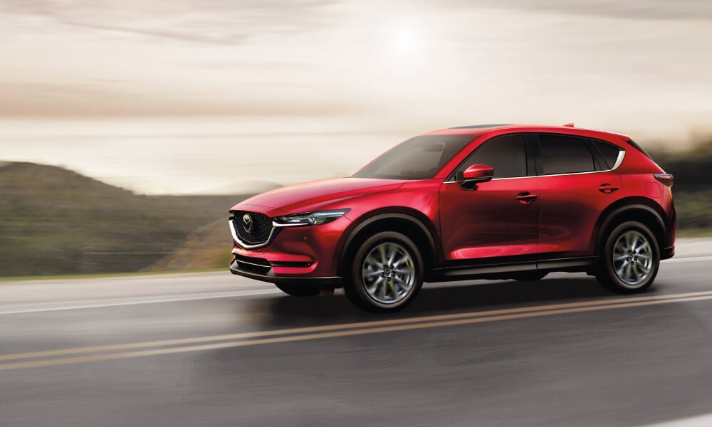 Red Mazda CX-5 on two-lane highway against hazy horizon and sky. 