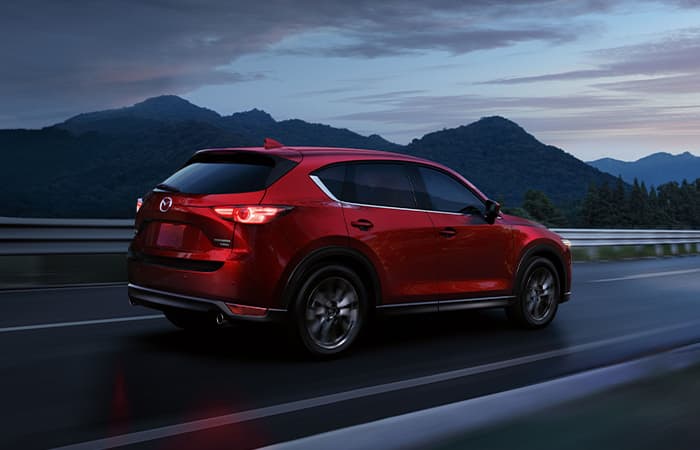 A red Mazda vehicle driving along a forest road.