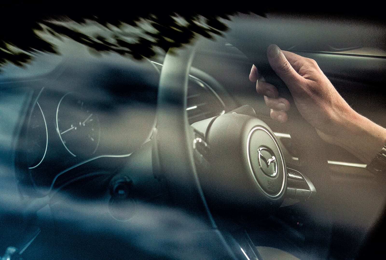 Main du conducteur sur le volant avec un logo Mazda.