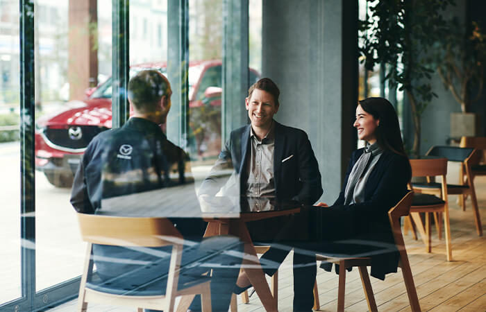 Smiling professional couple speaking with Mazda technician in coveralls in a Mazda Retailer’s office