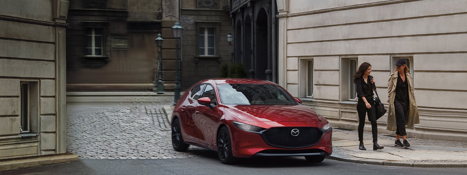 Femme longeant un VUS Mazda rouge stationné, près du mur de briques d’un édifice victorien