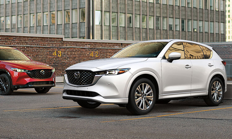 Rhodium White Metallic and Soul Red Crystal Metallic CX-5s parked on parking structures’ top floor in daylight. 