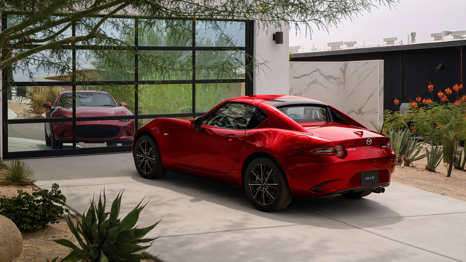 Une MX-5 RF rouge vibrant cristal métallisé garé devant un garage réfléchissant, mettant en valeur son design élégant dans une allée.