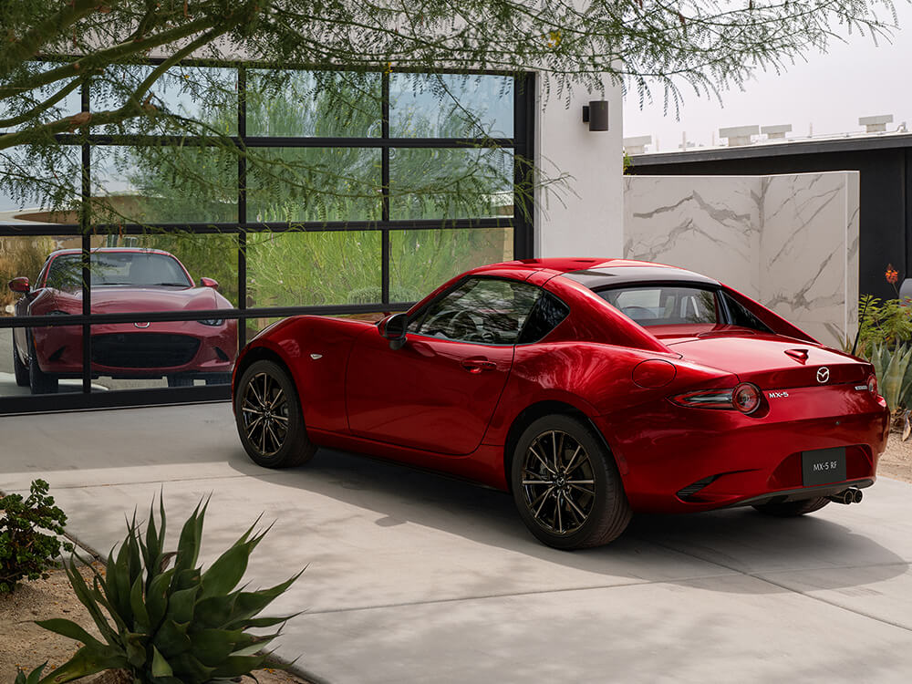 Une MX-5 rouge vibrant cristal métallisé stationnée dans une entrée; la porte du garage se reflète sur la voiture.