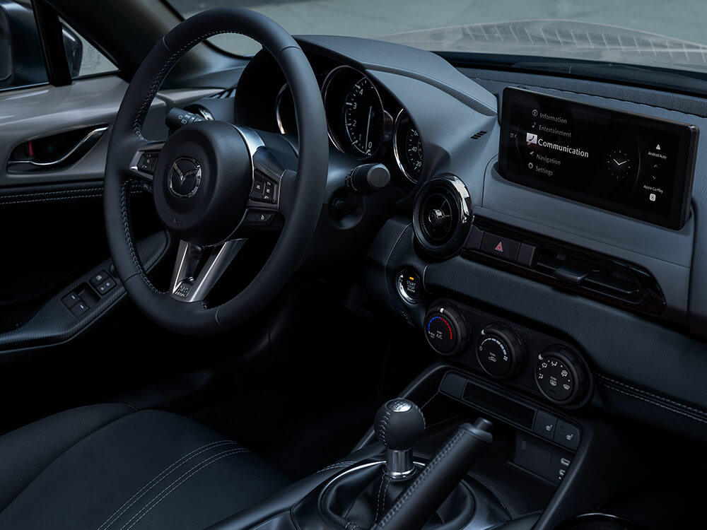 Vue à l’intérieur d’une MX-5 depuis le siège passager montrant les commandes de la console centrale et l’écran tactile.