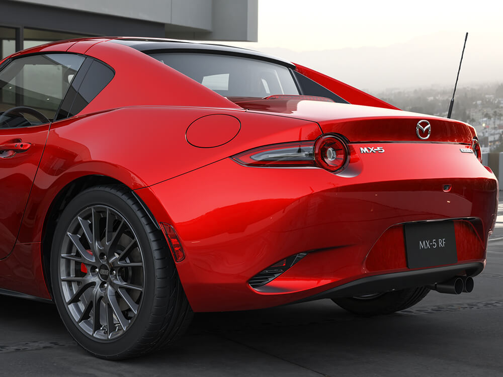 Gros plan sur le feu arrière gauche d’une Mazda MX-5 ST GS-P avec Groupe sport rouge vibrant cristal  reflétant les collines verdoyantes derrière. 