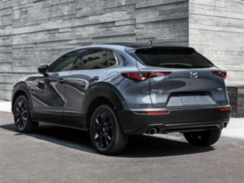 Profil de ¾ arrière d’un Mazda CX-30 gris mécanique métallisé garé devant des murs en pierre grise élégants et minimalistes. 