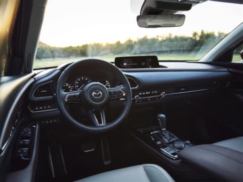 Vue du siège conducteur d’un CX-30 au crépuscule, mettant l’accent sur le volant, le tableau de bord, la console et les commandes des portes.  