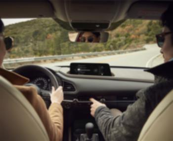 Un CX-30 circulant sur une route de montagne; vue intérieure à partir des sièges arrière vers le conducteur et le passager avant.