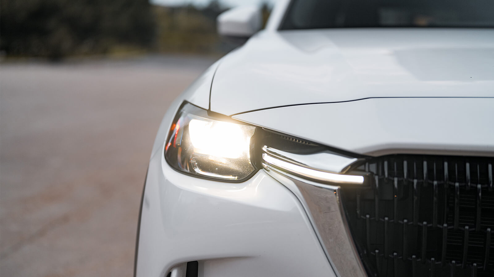 Straight on close up of front headlight and grille as well as sliver of hood and side of Artic White CX-90.  