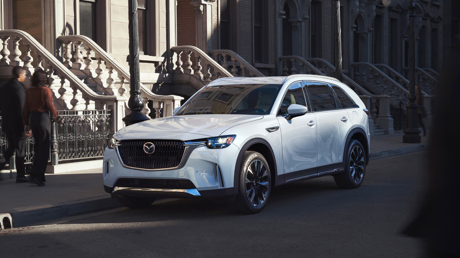 Arctic White CX-90 Parked along city street lined with regal concrete apartment stairs. 