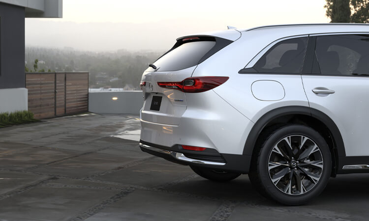 Profile of CX-90, rear half. Vehicle is parked in a stylish drive. 