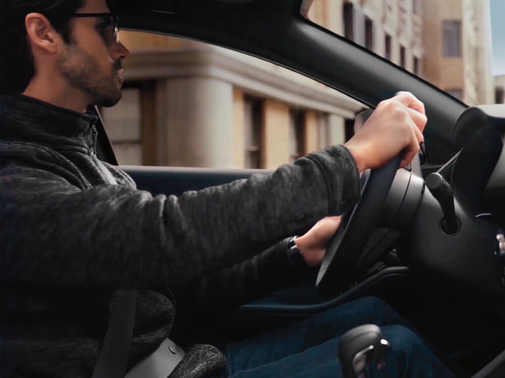 Close-up of male driver inside Mazda3 Sport making a turn. A stately building is blurred in background.